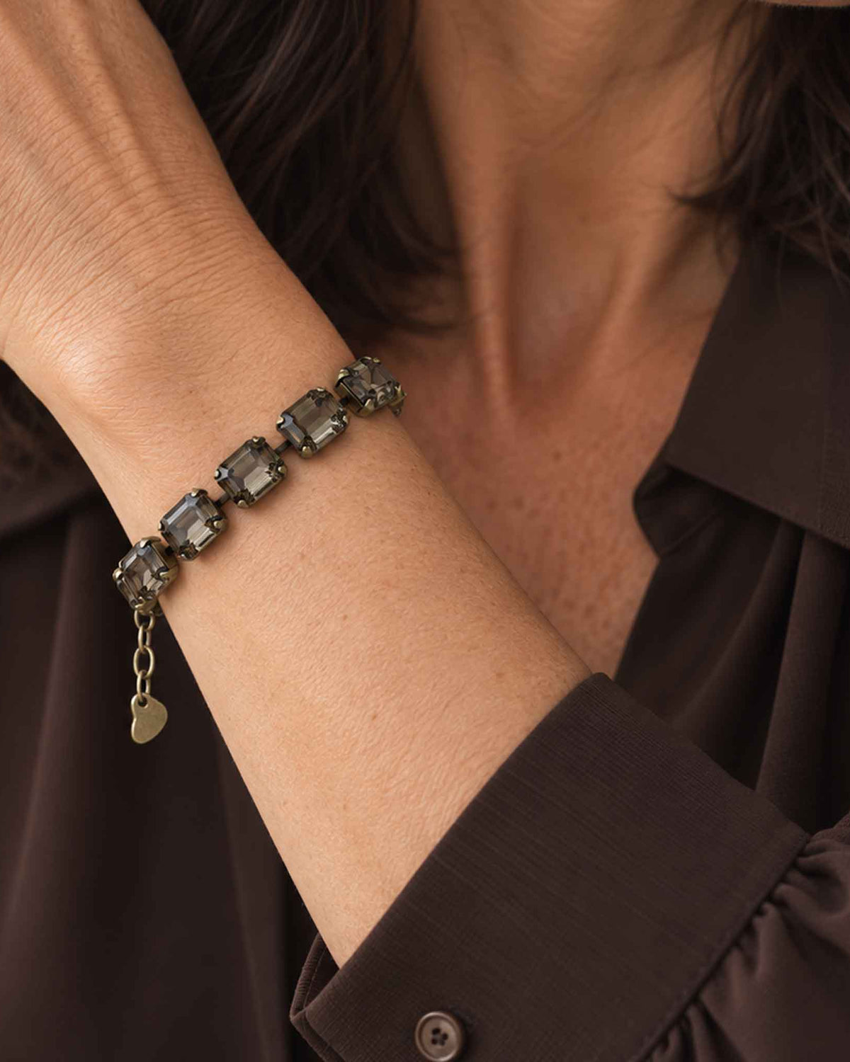 woman wearing emerald cut black diamond crystal bracelet with antique brass with a brown colored blouse.
