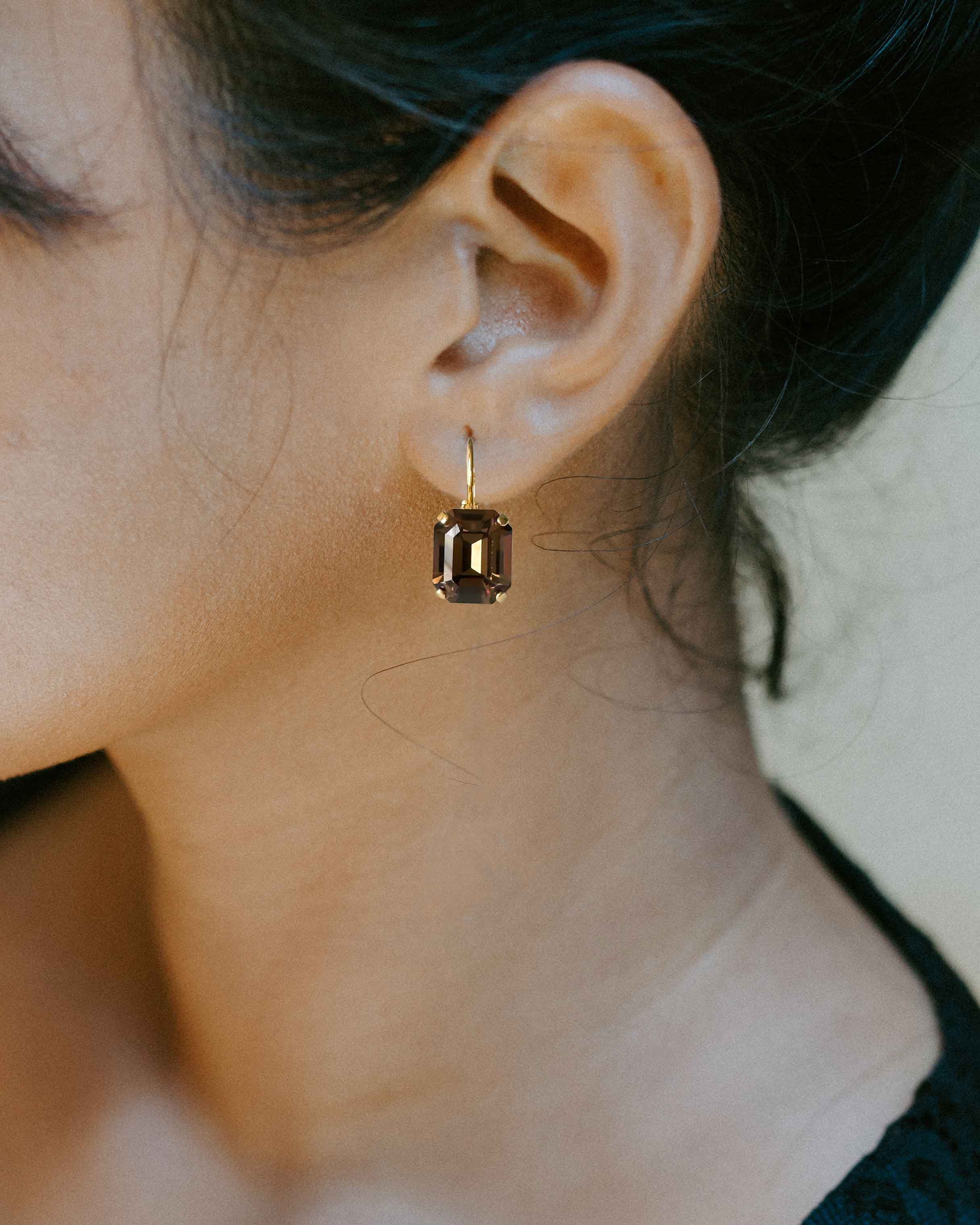 Woman wearing small rectangular drop brown rhinestone earrings.