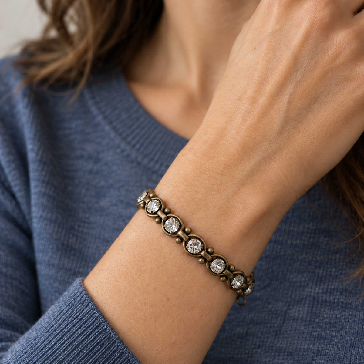 woman wearing clear crystal and antique brass link bracelet with a blue sweater.