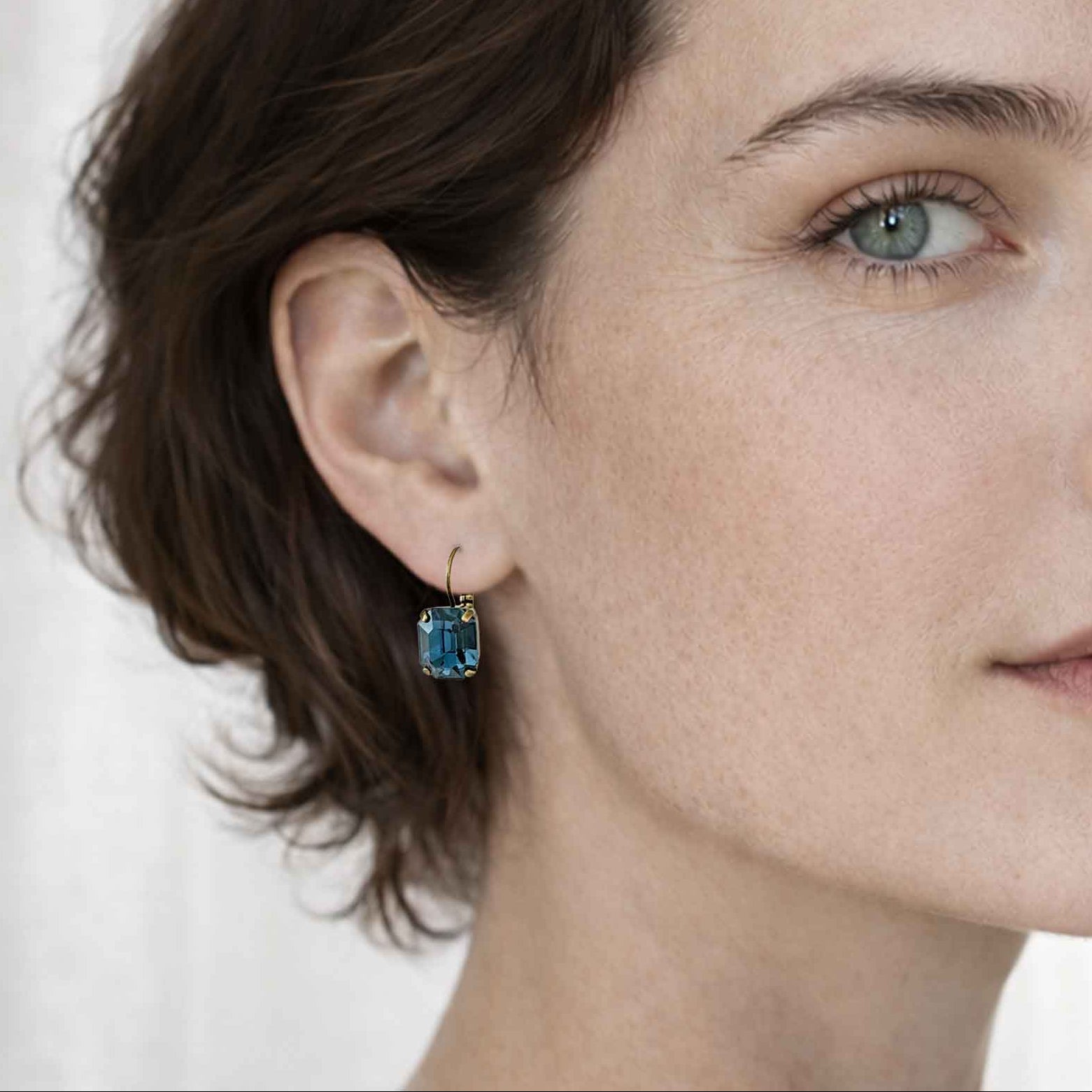 Closeup of a woman wearing deep blue crystal rhinestone earrings by Petite Margaux.