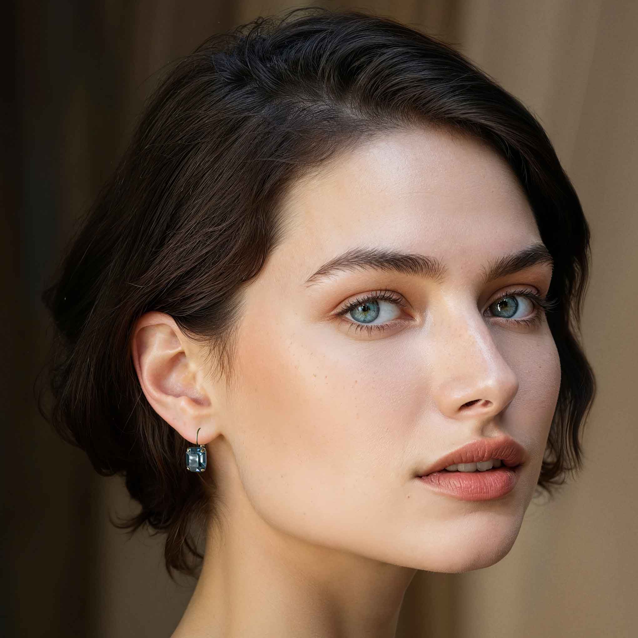 Young brunette women with blue eyes wearing matching blue, emerald cut earrings of fine cut crystal from Europe.