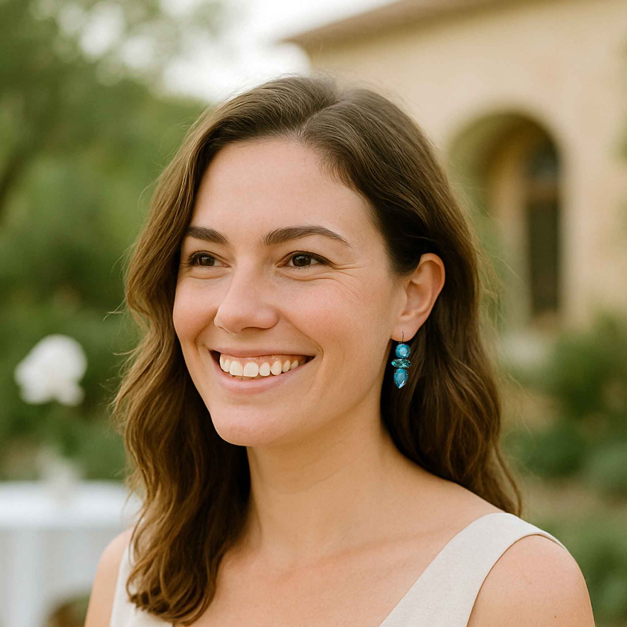 Young woman wearing aqua turquoise statement earrings by Petite Margaux at a Winery in a white linen dress.