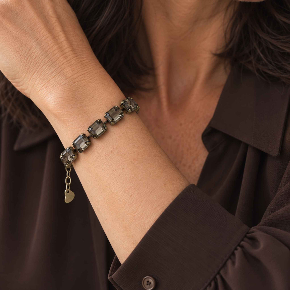 woman wearing emerald cut black diamond crystal bracelet with antique brass with a brown colored blouse.