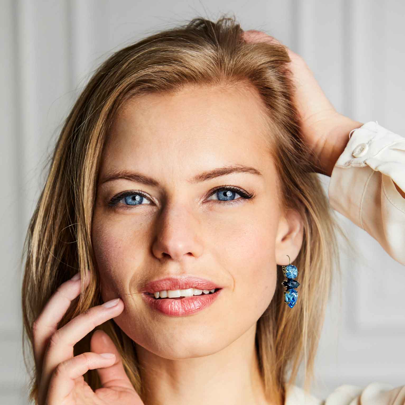 Woman modeling blue crystal statement earrings by Petite Margaux.