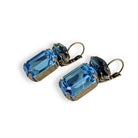 Angled view of antique brass and blue crystal earrings with dark and lighter blue crystals.