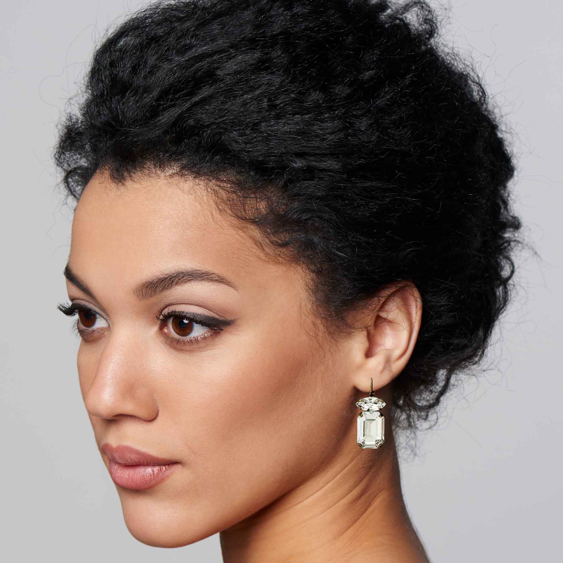 Woman wearing emerald cut clear crystal drop earrings.