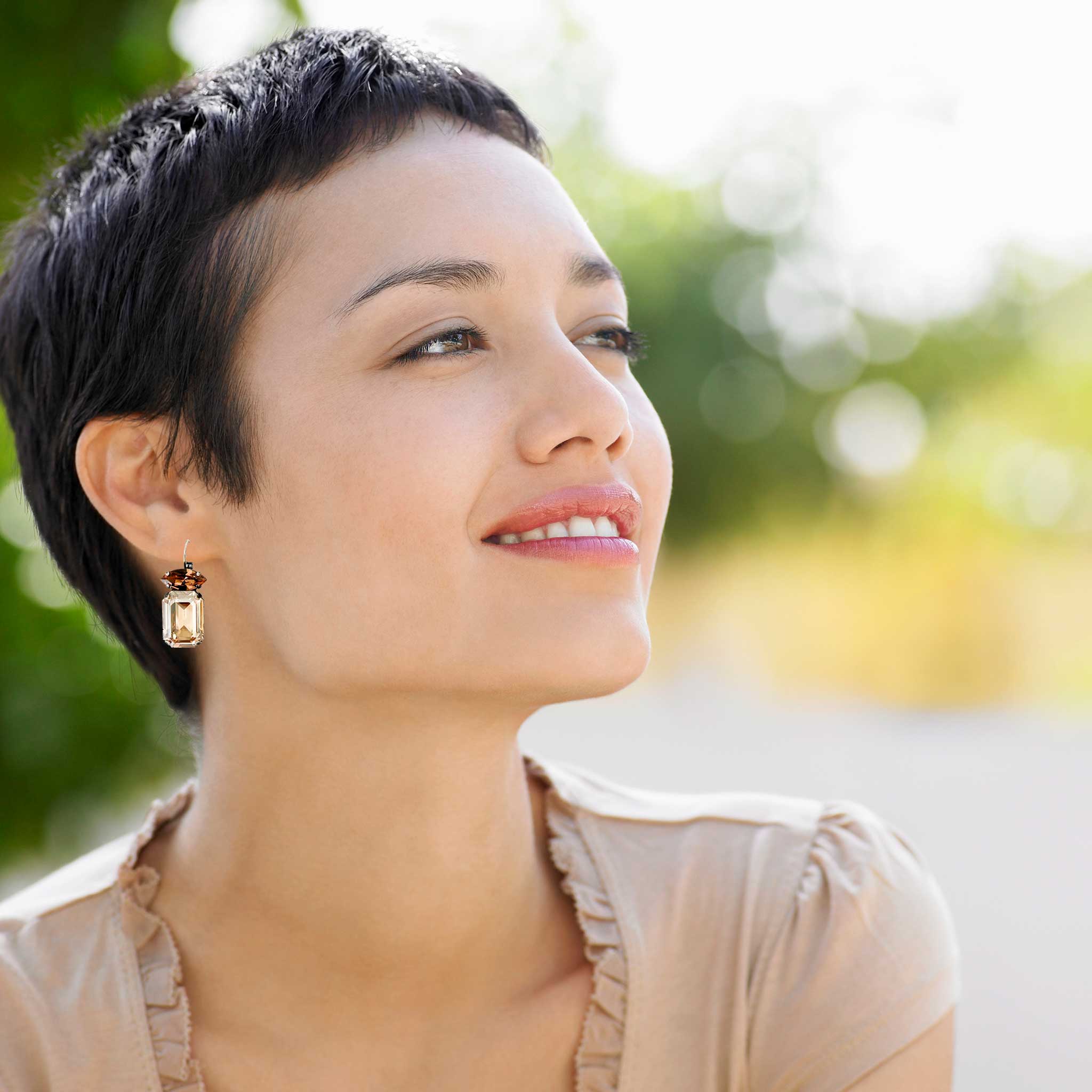 Young asian women wearing brown and golden topaz colored crystal earrings by Petite Margaux.