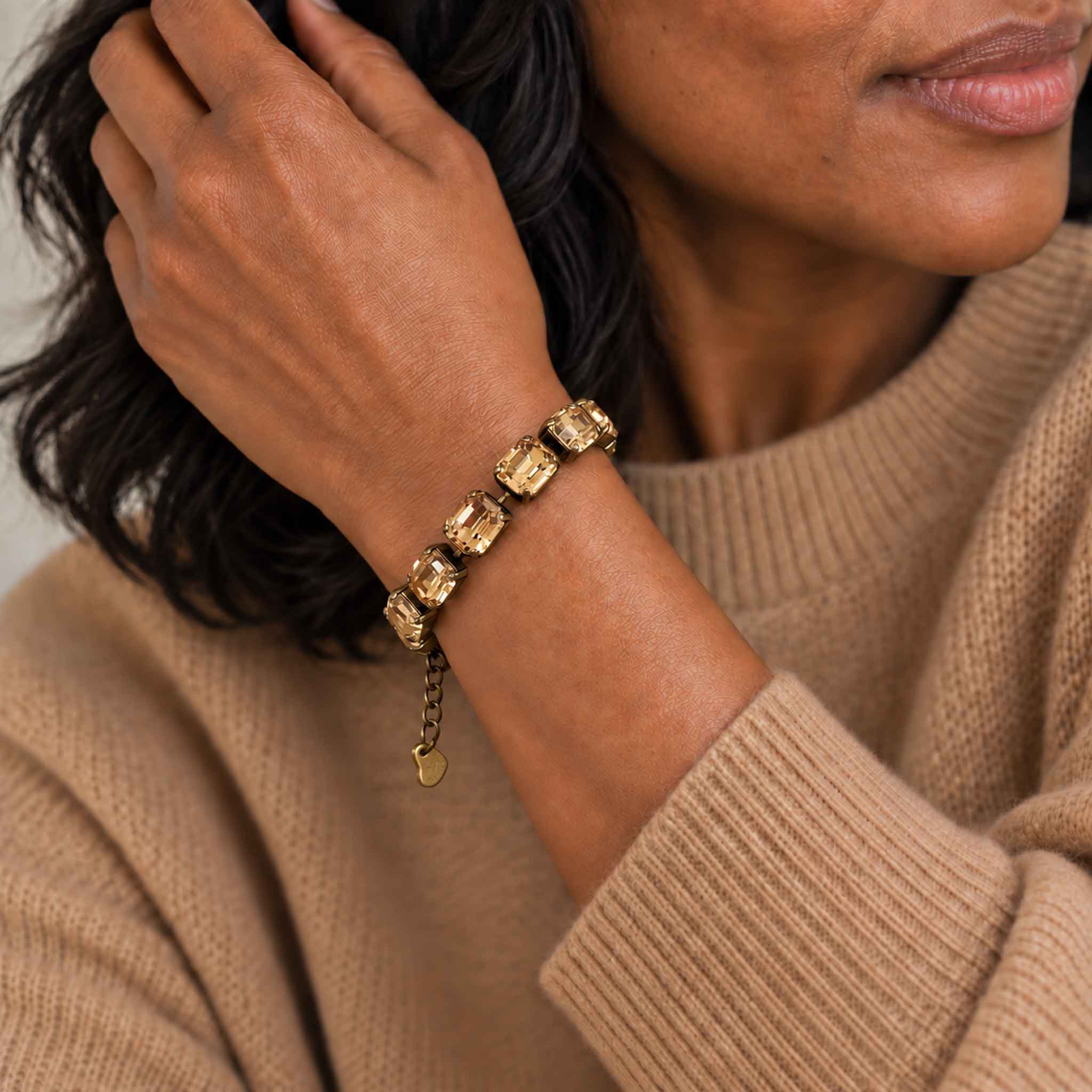 Stylish black woman wearing light topaz crystal bracelet with a camel colored cashmere sweater. The bracelet has emerald cut stones that are set in antique brass.