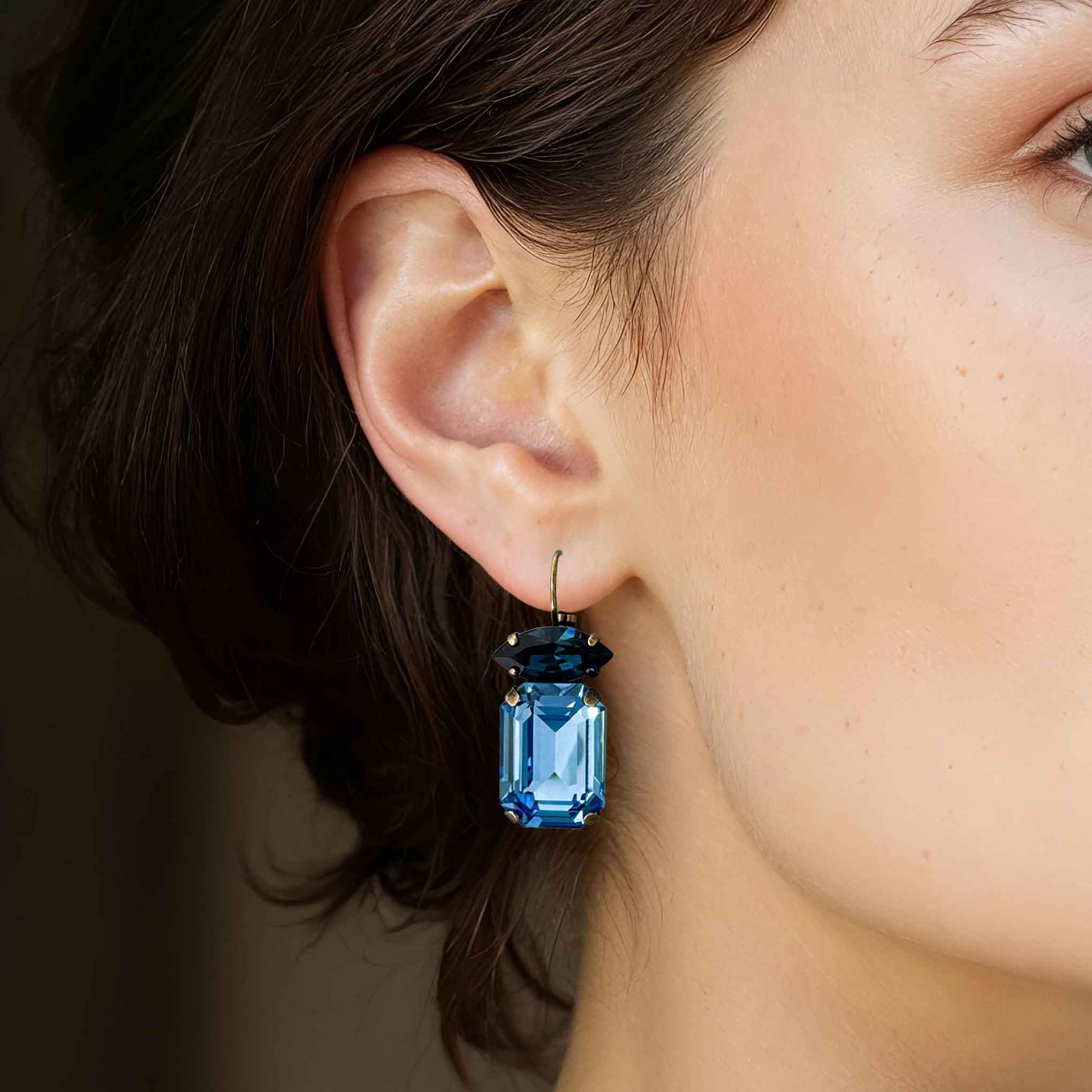 Closeup view of a woman wearing blue crystal drop earrings by Petite Margaux.