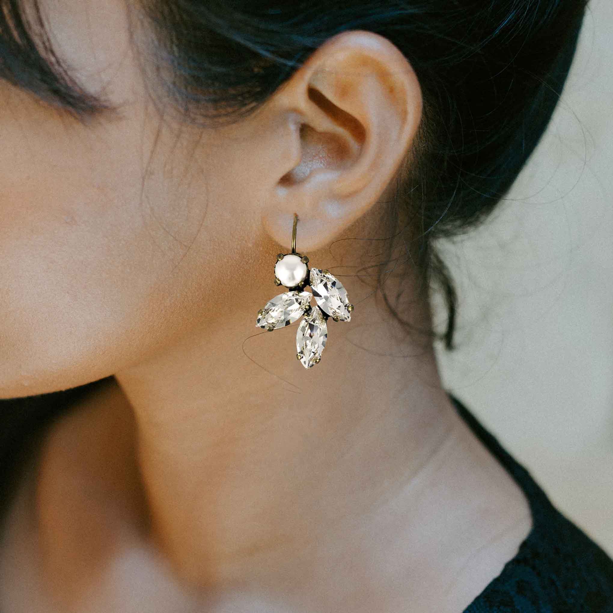 Woman wearing leaf motif clear crystal and pearl rhinestone earrings.