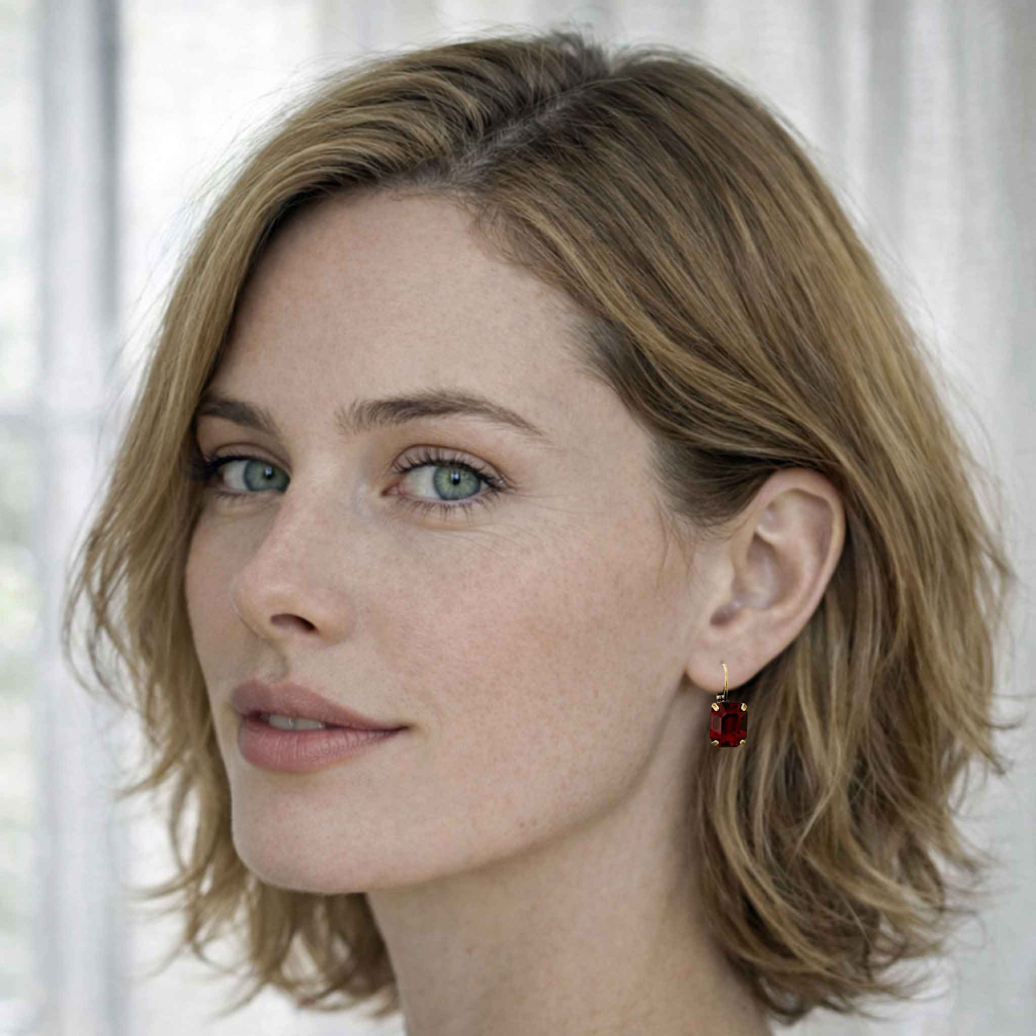 Close-up of a woman with light brown hair and freckles, wearing a red crystal earring.